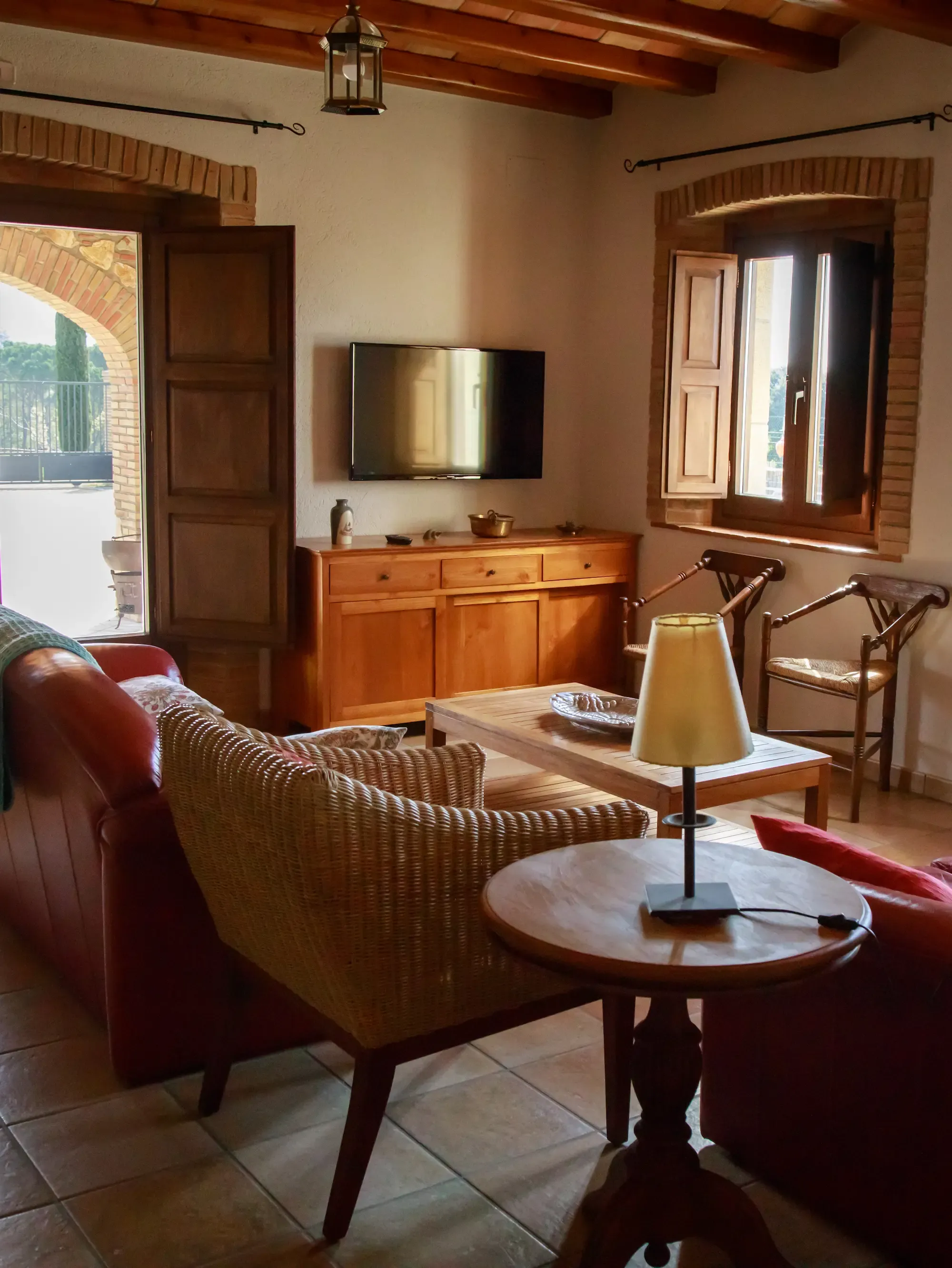 Un saló lluminós amb vigues de fusta, rajoles de terracota, seients de vímet i cuir, una taula de cafè i un televisor de pantalla plana.